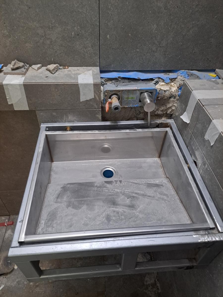 벽 타일 일부를 열고 세면대 프레임과 배관을 확인하는 단계